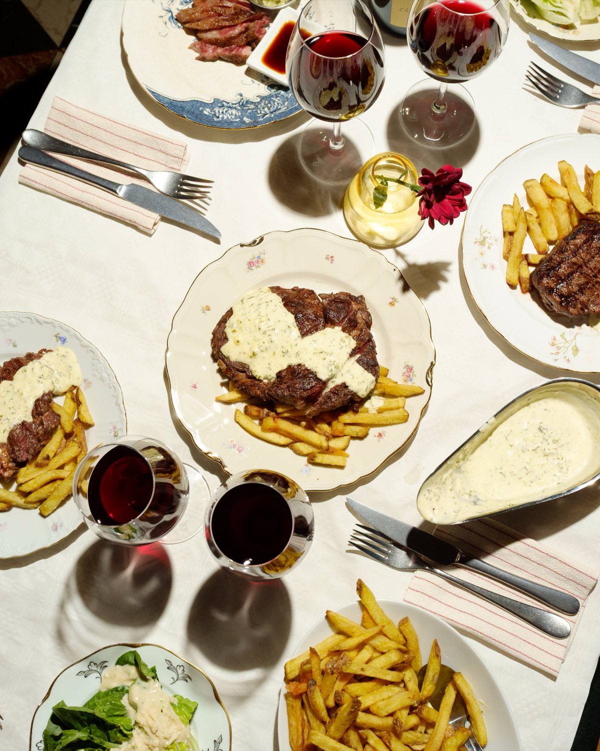 Steak frites på blommigt porslin — entrecôte, sås och pommes, uppdukat med rödvin