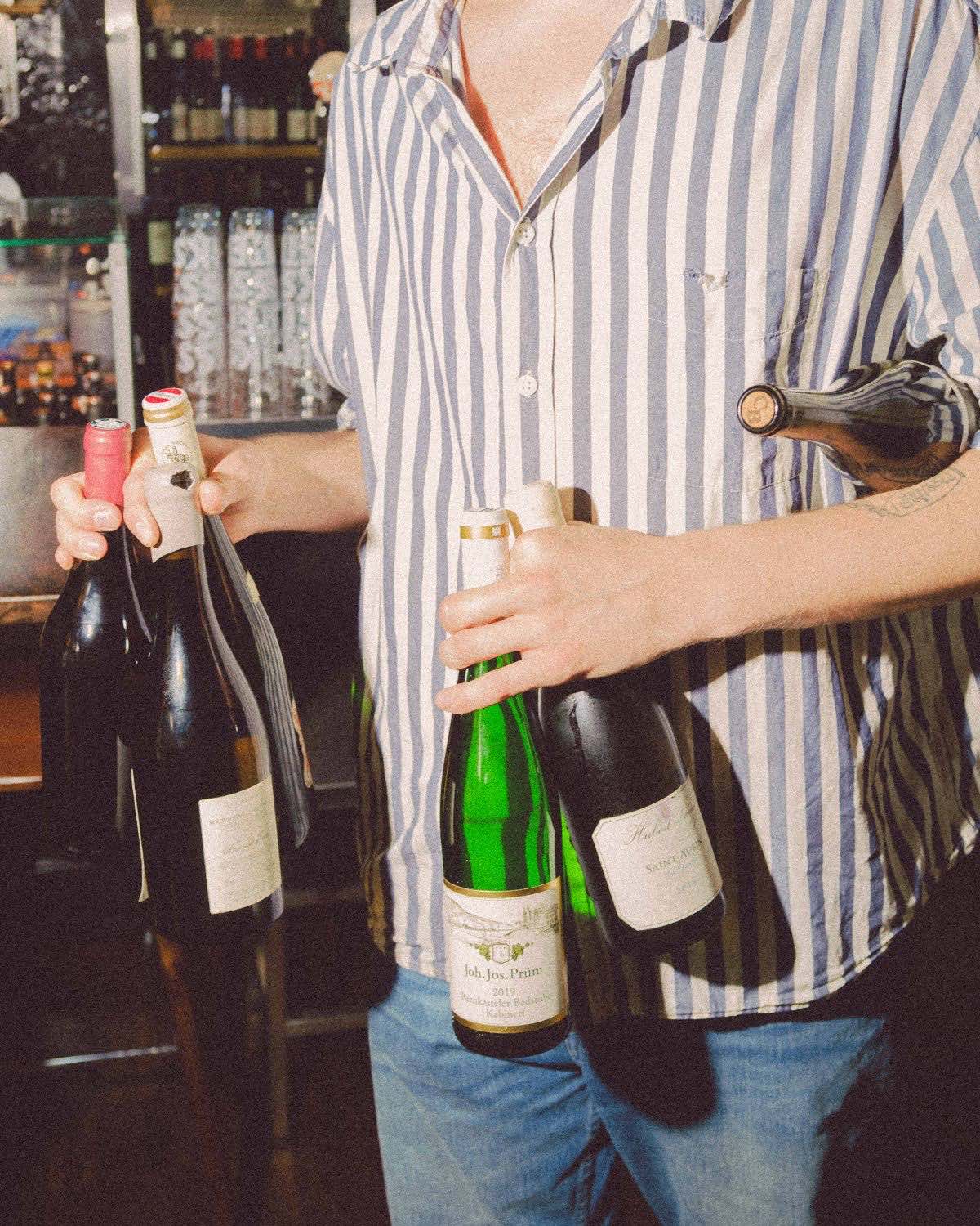 En flaska vitt vin sänks ner i en isfylld vinkylare, framför franska vinaffischer.