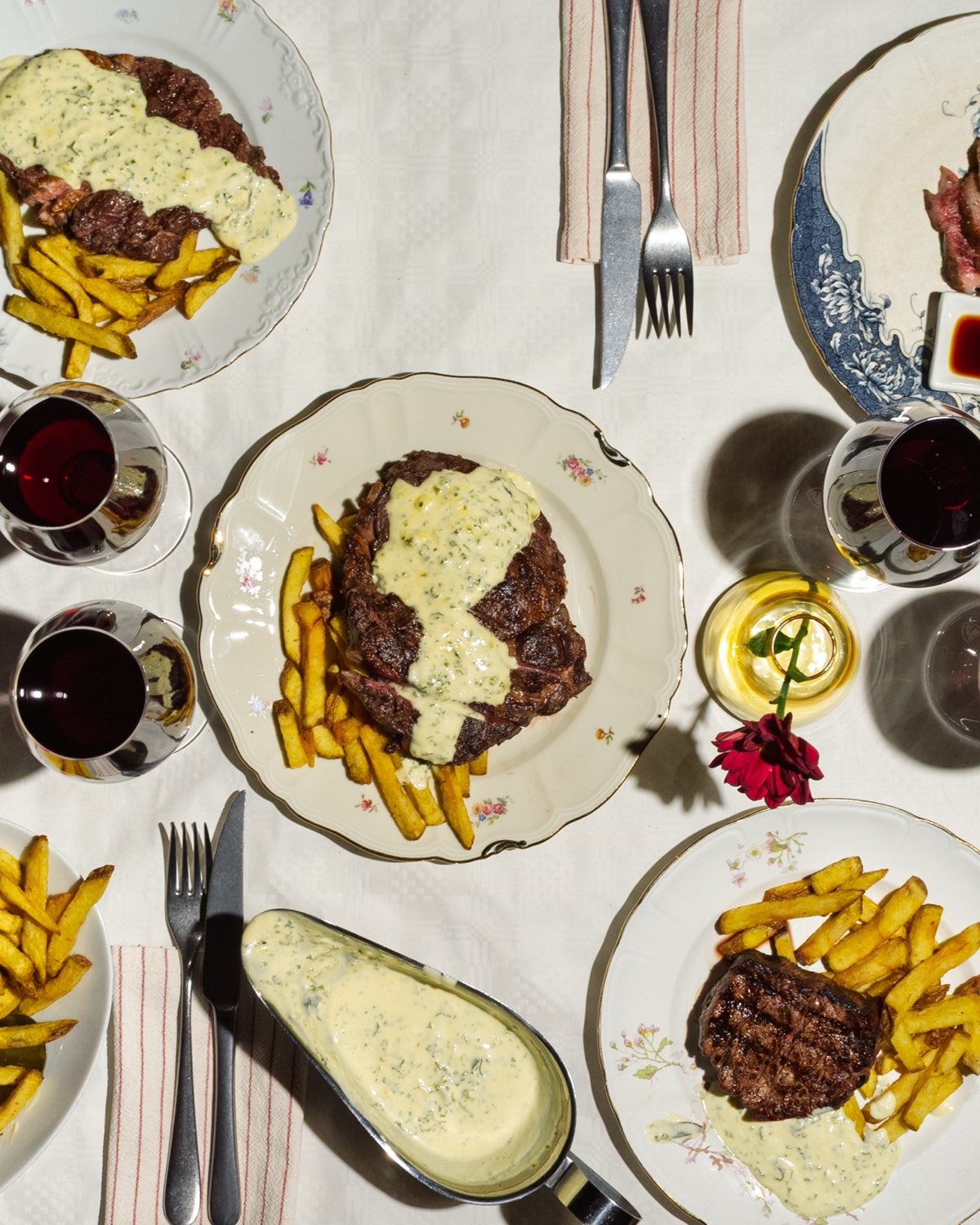 Dukat bord ovanifrån — flera tallrikar steak frites med pommes, sås och rödvin.